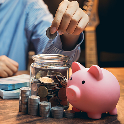Person putting money into a jar next to a piggy bank.